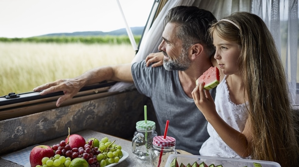Father with daughter eating watermelon in a caravan looking out of window